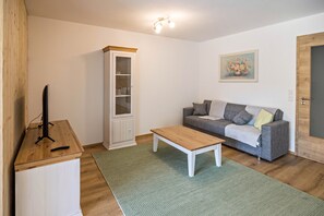 Una sala de estar con una mesa de centro de madera, un sofá gris, un mueble blanco y un cuadro en la pared.