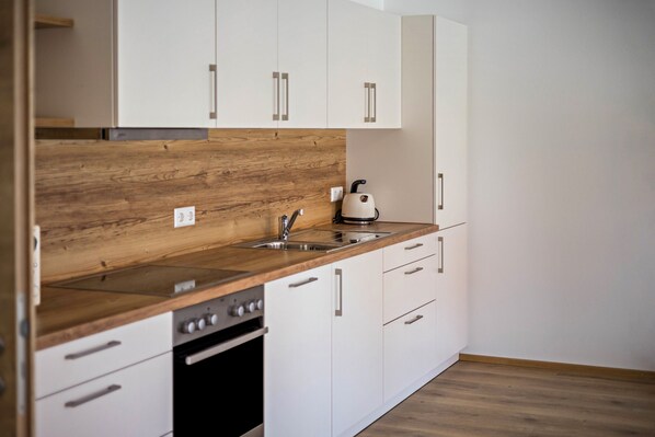 A modern kitchen with white cabinets, a wooden countertop, a built-in oven, and a kettle.