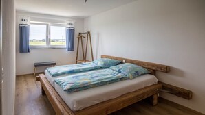 Una habitación con una cama de madera, un banco, una ventana con cortinas y vistas al exterior.