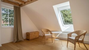 A room with a sloped ceiling, a wooden chest of drawers, two wicker chairs, a small table, and a window with a view of trees. - "Holiday cottage Fischbach" close to the Lake with Wi-Fi (Friedrichshafen)