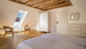 A bedroom with a sloped ceiling, a skylight, a bed with striped bedding, a wardrobe, and a chair. - "Holiday cottage Fischbach" close to the Lake with Wi-Fi (Friedrichshafen)