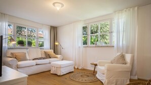 A room with a white sofa set, a small side table, a wicker chair, and a round rug. - "Holiday cottage Fischbach" close to the Lake with Wi-Fi (Friedrichshafen)