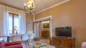 A living room with red leather sofas, a glass coffee table, a TV on a wooden cabinet, and a dining area with a table and chairs. - Miranda by Interhome (Volterra)