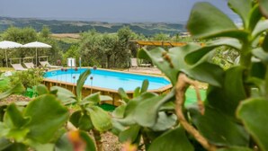 A swimming pool with lounge chairs and umbrellas, surrounded by greenery and hills in the background. - Miranda by Interhome (Volterra)