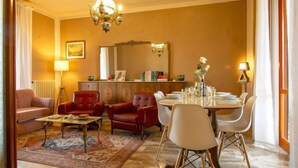 A living room with a sofa, two armchairs, a coffee table, a dining table set for four, and a chandelier. - Miranda by Interhome (Volterra)