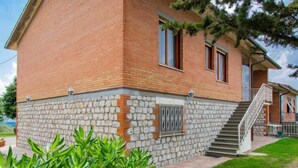 A two-story building with a stone foundation and red brick walls, featuring a staircase leading to the upper floor. - Miranda by Interhome (Volterra)