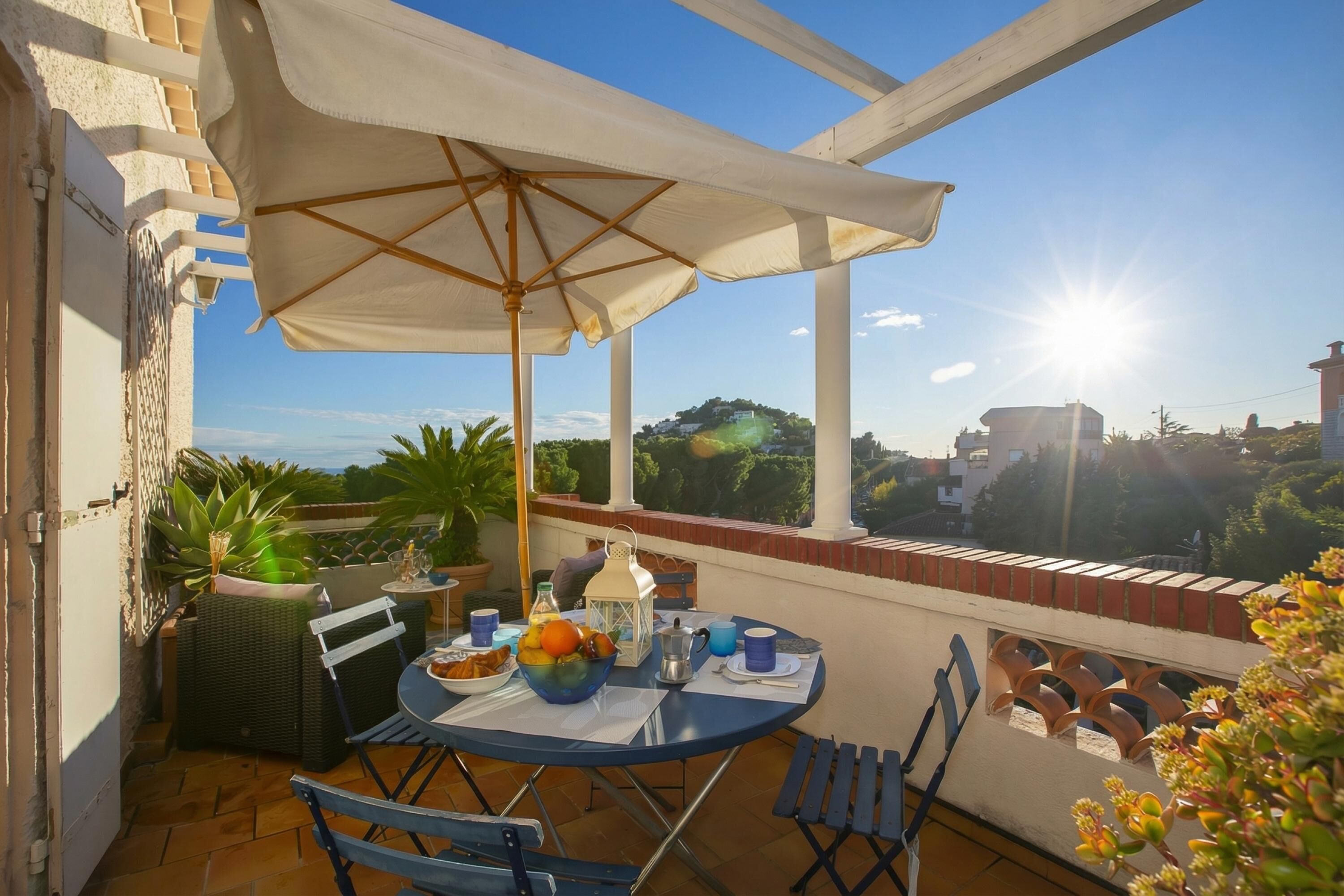 A balcony with a table set for breakfast, a white umbrella, and a view of the surrounding landscape.