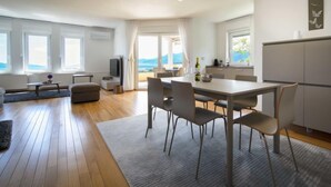 Un salon moderne comprenant un coin repas, une cuisine et de grandes fenêtres donnant sur la mer.