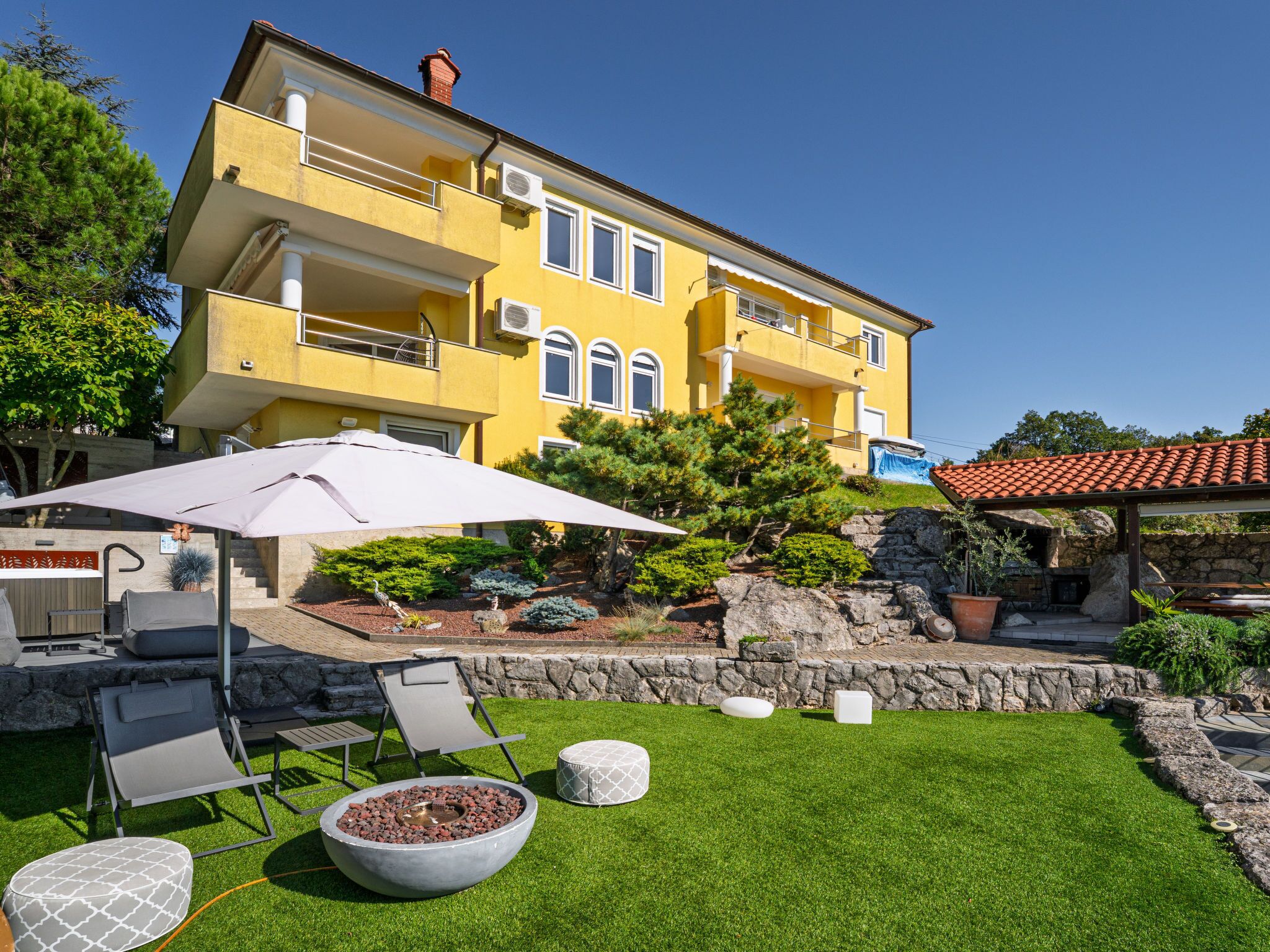 A yellow building with a balcony, outdoor seating, and a fire pit.
