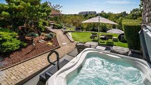 Un bain à remous doté d’une terrasse en bois, entouré d’un jardin aménagé avec différentes plantes et d’un espace patio agrémenté de mobilier d’extérieur.