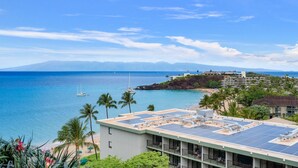 Un hôtel situé sur la côte, doté d’une installation de panneaux solaires sur le toit, offrant une vue sur la plage et ayant une chaîne de montagnes en arrière-plan.