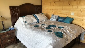 Un lit bien fait, avec une literie à motifs floraux, une tête de lit en bois et une table de chevet sur laquelle se trouvent une lampe et une boîte de mouchoirs.