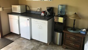 Une cuisine compacte équipée d’un four à micro-ondes, d’une machine à café, d’un distributeur d’eau et d’un petit placard.