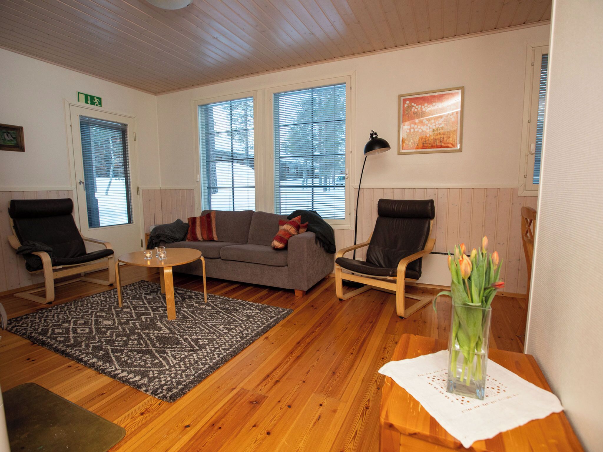 A cozy living room with a grey sofa, two black chairs, a small coffee table, and a patterned rug.