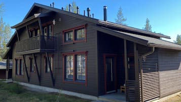 A two-story wooden house with a balcony, large windows, and a chimney.