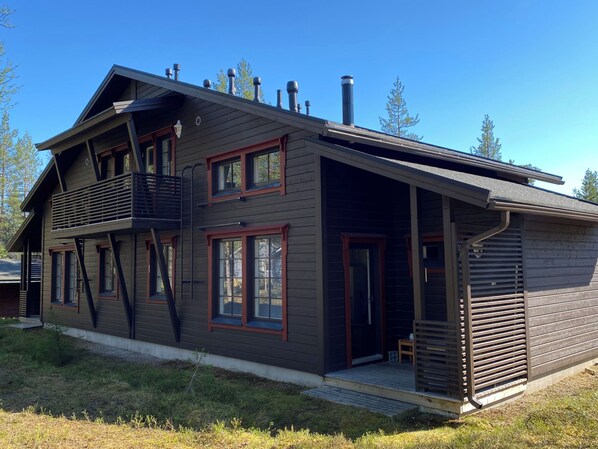 A two-story wooden house with a balcony, large windows, and a chimney.