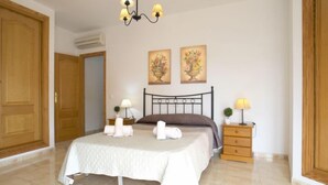 Een slaapkamer met een bed, twee nachtkastjes, een kroonluchter en twee aan de muur bevestigde schilderijen.