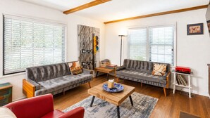 Ein Wohnzimmer mit zwei grauen Sofas, einem roten Sessel, einem Holztisch und einem Bücherregal.