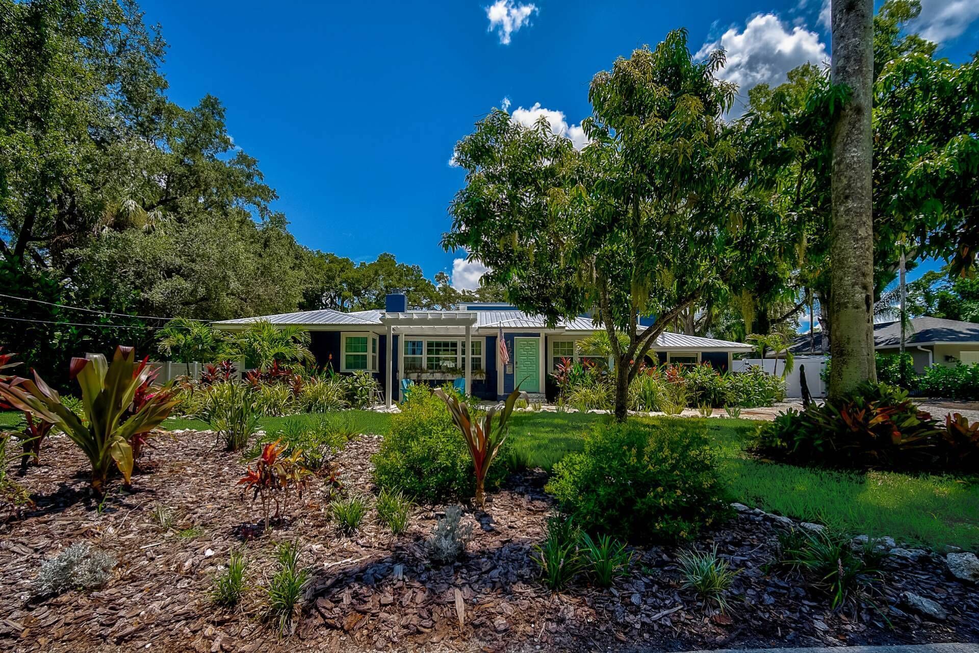 A house with a garden, surrounded by trees and a clear blue sky.