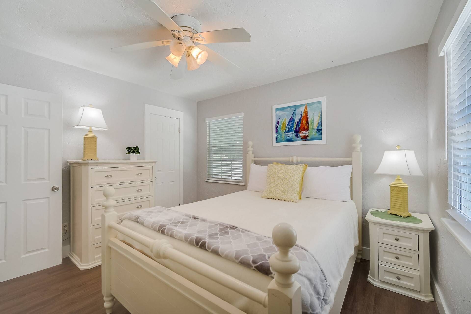 Une chambre à coucher avec un lit, un ventilateur de plafond, une table de chevet avec une lampe, une commode et un tableau au mur.