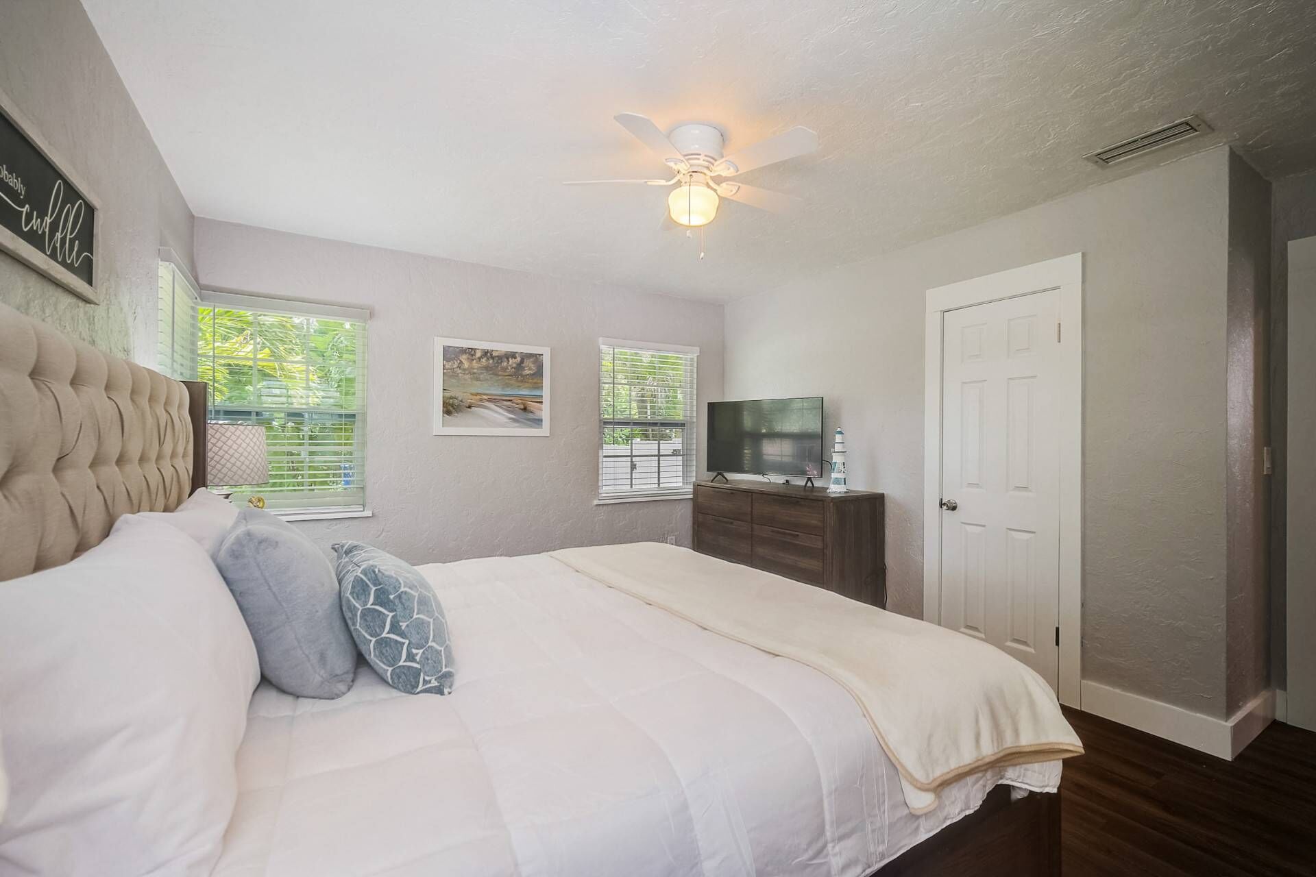 A bedroom with a bed, a ceiling fan, a TV, and a door.