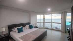 A bedroom with a large bed, a nightstand, a window with a view of the sea, and a balcony with a railing. - Gorgeous views, 2 rooms, AC, Pool, beach, hot showers! (Cartagena)