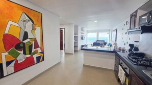 A modern kitchen with a gas stove, a microwave, and a coffee maker. There is a large abstract painting on the wall and a view of the ocean through the window. - Gorgeous views, 2 rooms, AC, Pool, beach, hot showers! (Cartagena)