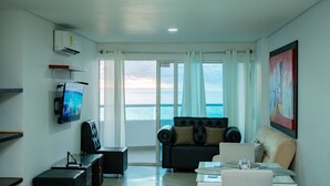 A living room with a sofa, a coffee table, and a TV. There is a view of the ocean through large windows. - Gorgeous views, 2 rooms, AC, Pool, beach, hot showers! (Cartagena)