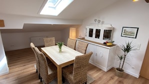 A dining area with a wooden table and wicker chairs, a white cabinet with glass doors, and a skylight above.