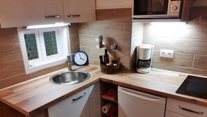 Una cocina compacta con un lavamanos, un reloj, una cafetera y un microondas.