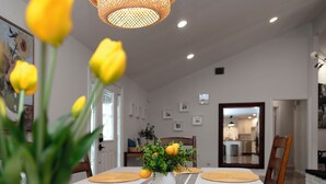 Un comedor con una mesa dispuesta para cuatro personas, un jarrón con flores amarillas y una lámpara de araña moderna.