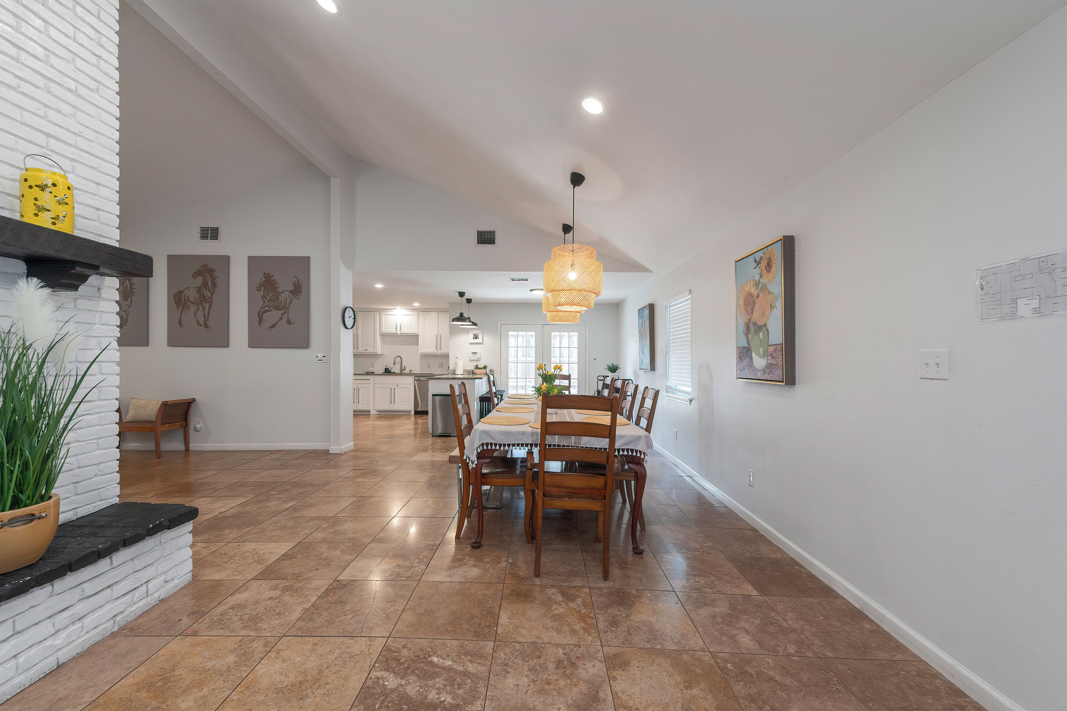 A spacious kitchen with white cabinets, a dining area with a wooden table and chairs, and a hanging light fixture.