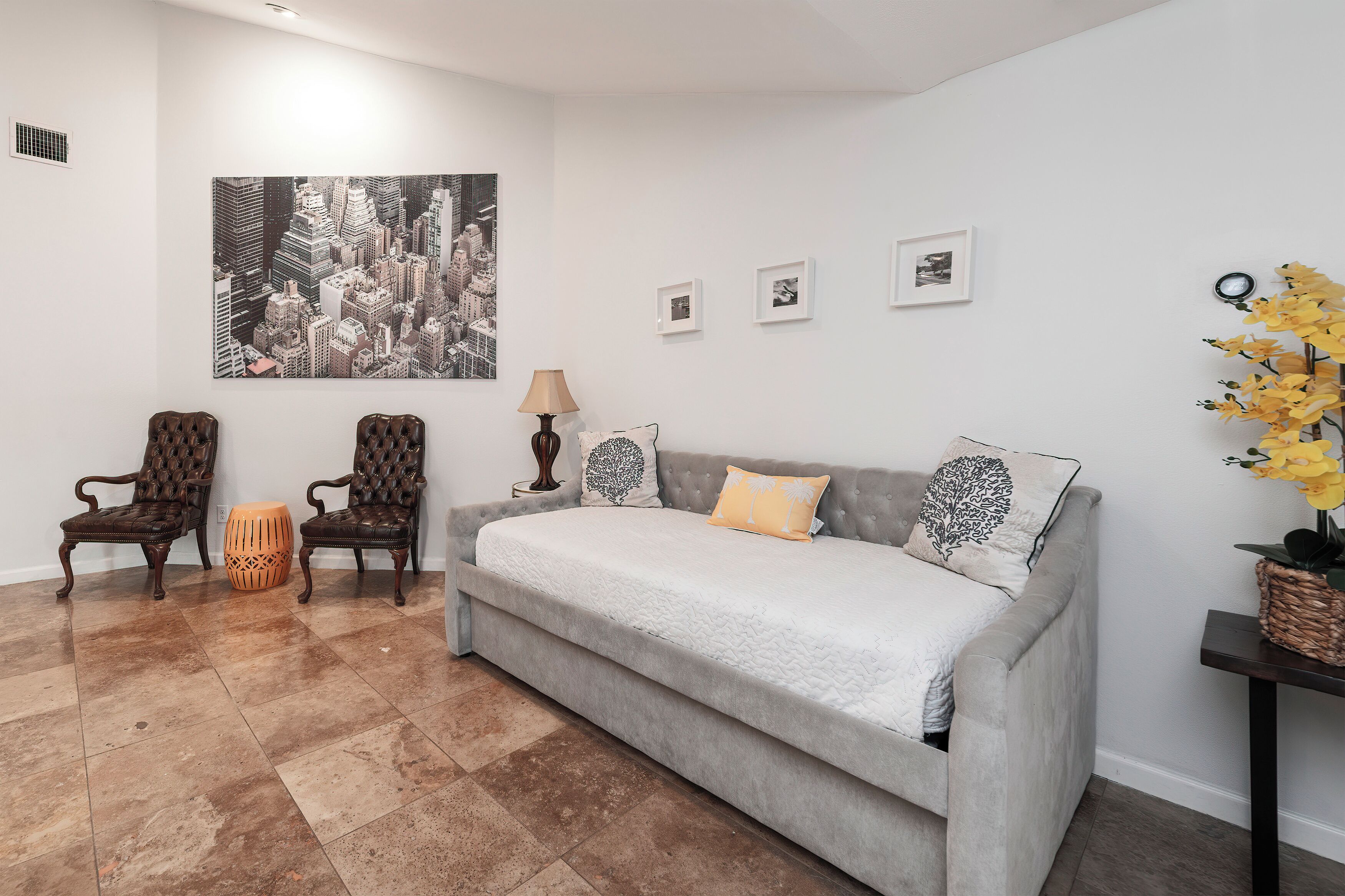 Un salon moderne avec un canapé gris, deux fauteuils, une petite table d’appoint et un grand tableau représentant un paysage urbain accroché au mur.