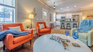 A living room with two orange armchairs, a white coffee table, and a kitchen in the background.
