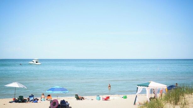 A beach with people relaxing under umbrellas, a tent, and a boat in the water.