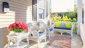 A porch with wicker chairs, a potted plant, and a colorful rug.