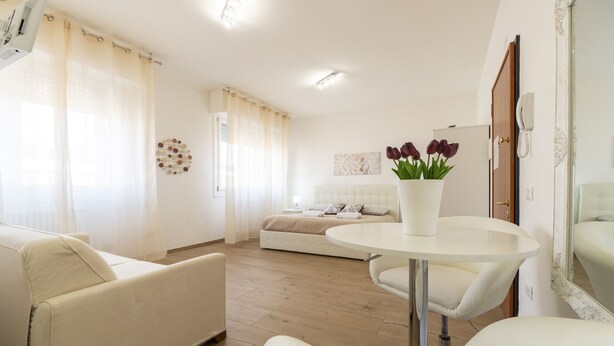 A modern living room with a round white table, a sofa, and a bed in the background. - Liberty Fiera Bologna (Bologna)