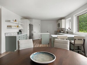 A modern kitchen with white cabinetry, a central island, and a dining area with a wooden table and chairs. - Private Mountain View Home on 2 Acres in Bozeman (Bozeman)