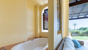 A bathroom with a large bathtub, a window with decorative glass, and a view of a garden and palm tree. - Lovely and comfortable apartment in Altea, on the Costa Blanca, Spain  with communal pool for 4 persons (Altea)