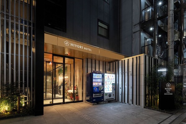 Exterior del hotel Hiyori, con una máquina expendedora y un cartel que indica su ubicación en Osaka.