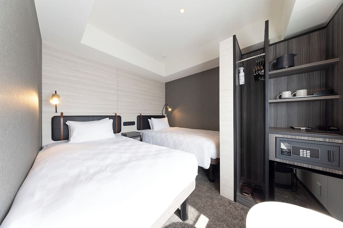 Ein modernes Hotelzimmer mit zwei Betten, einem Schreibtisch und einer integrierten Minibar.