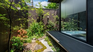 A modern outdoor space with a wooden fence, lush greenery, a small stream, and a hot tub. - Souhi Machiya House (Kyoto)