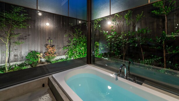 A modern bathroom with a large bathtub, wooden paneling, and a view of a garden. - Souhi Machiya House (Kyoto)
