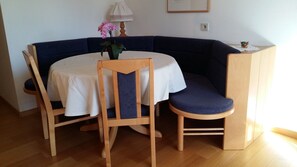 Un coin repas avec une table ronde, deux chaises, un vase de fleurs, une lampe et un tableau encadré au mur.
