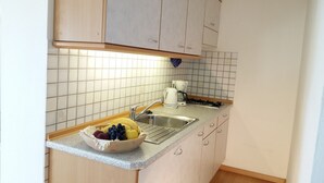 Et lille køkken med vask, kaffemaskine og en skål med frugt på disken.