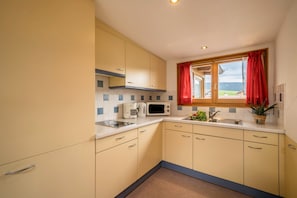 A kitchen with a microwave, sink, and window with red curtains.