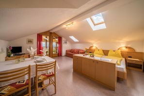 A cozy, well-lit room with a dining table, a sofa, a bed with yellow pillows, and a TV.