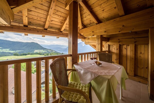 A wooden balcony with a table and chairs, overlooking a mountainous landscape.