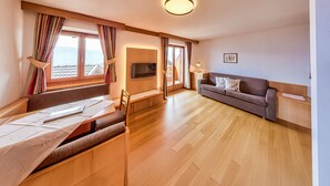 Una habitación con mesa de comedor, sofá, televisión y ventanas amplias.