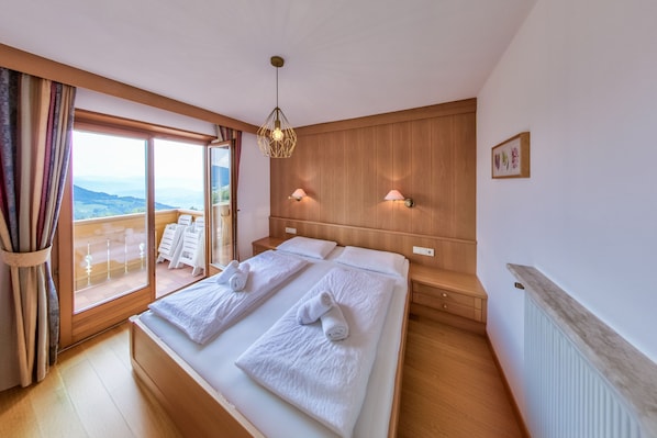 Une chambre d’hôtel avec deux lits, une grande fenêtre donnant sur un beau paysage, une tête de lit en bois et un luminaire au plafond.